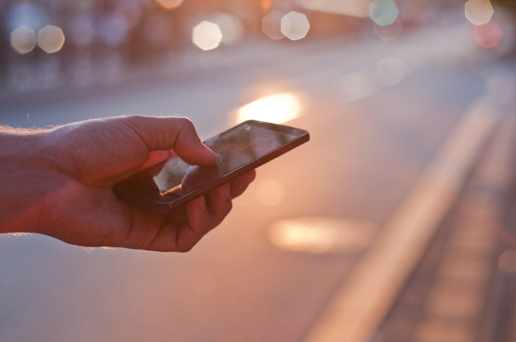 Man using mobile smartphone. Close up of a businessman hand holding and using a smart phone outdoors. Detail of handsome hipster modern businessman using smart phone in the city